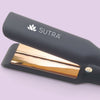 a close-up image of a black flat iron, the gold color plate measuring one and a half inches, gold color details, and the white sutra logo
