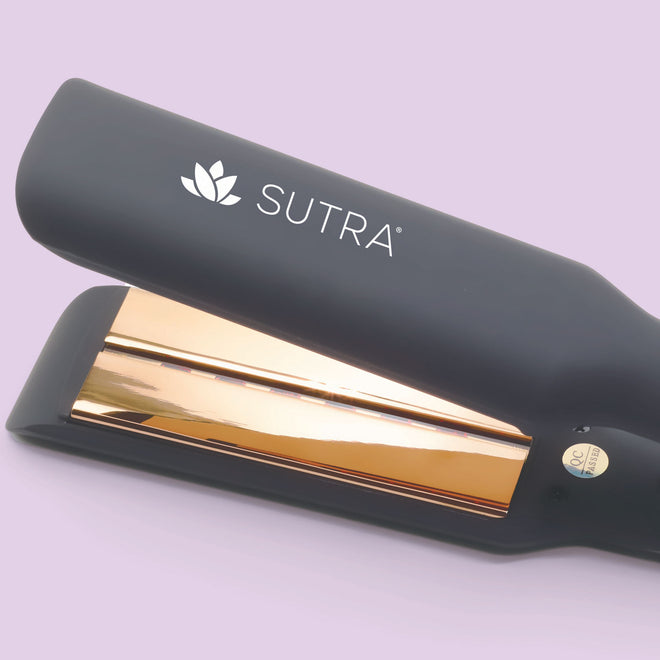 a close-up image of a black flat iron, the gold color plate measuring one and a half inches, gold color details, and the white sutra logo